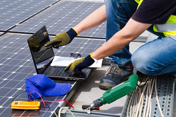 A technician kneeling on a solar array with a laptop and a multimeter, commissioning it